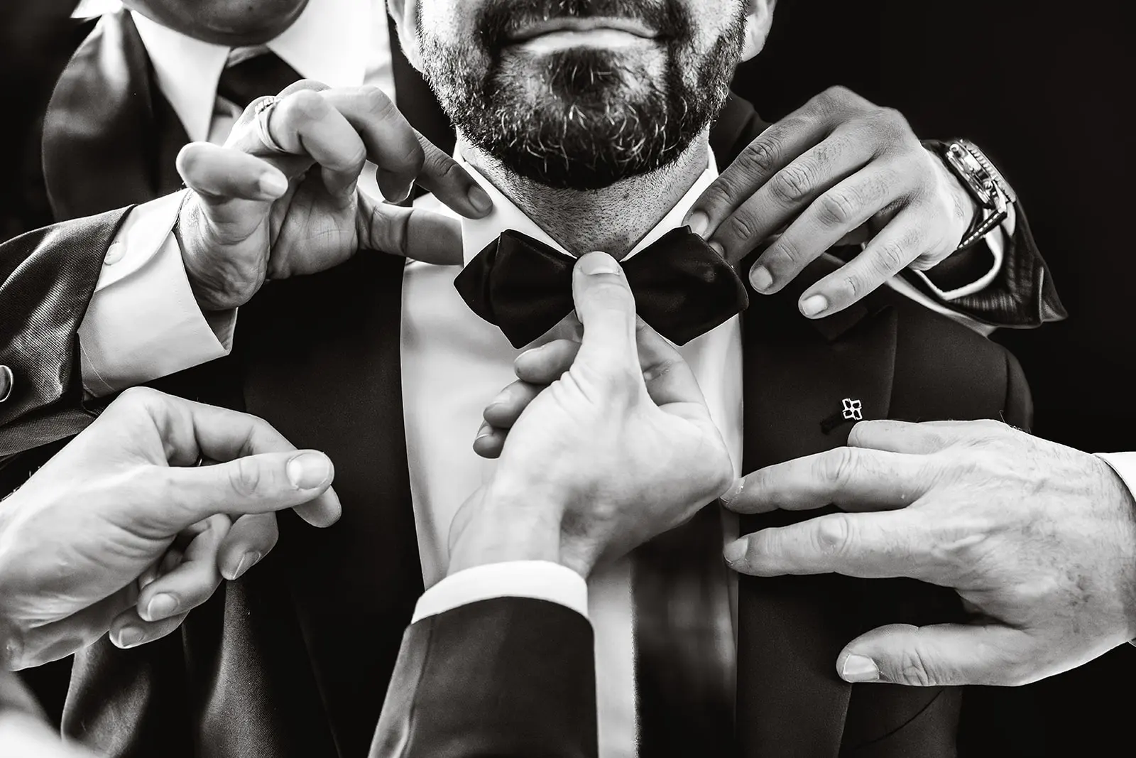 The groom adjusting his bow tie, in black and white