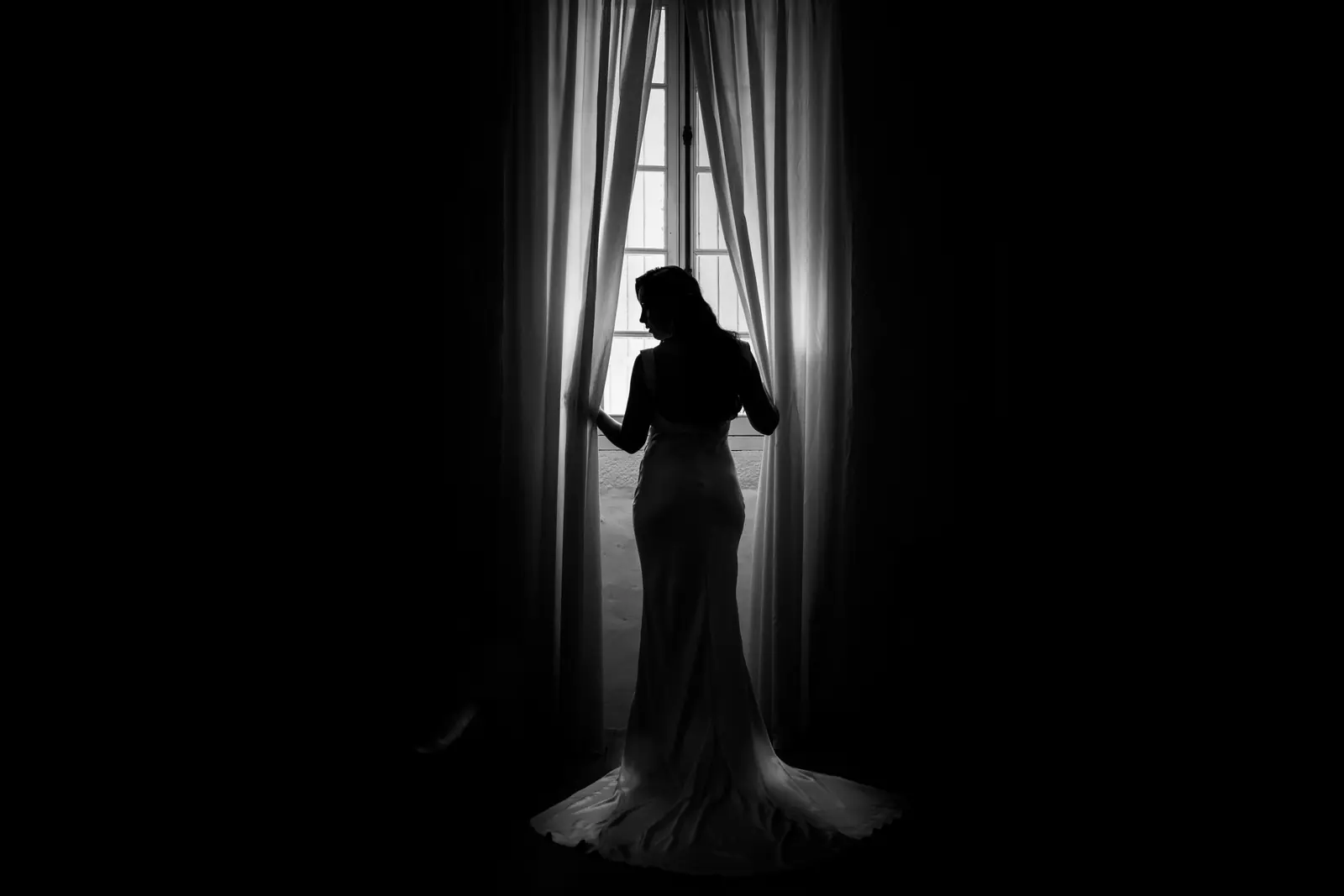 Silhouette de la mariée devant une fenêtre, en clair-obscur